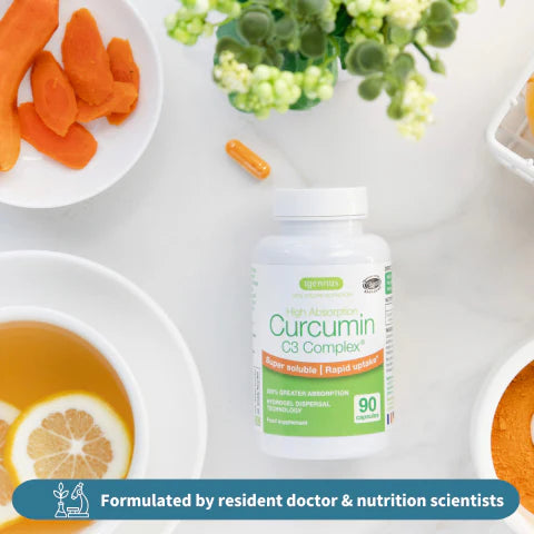 Supplement bottle labeled 'Curcumin C3 Complex' on a table with carrots, lemon, and tea.