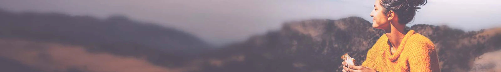 Person in an orange sweater standing on a mountain with a scenic view