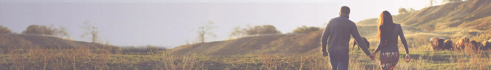 Two people walking hand in hand across a grassy field with a scenic background
