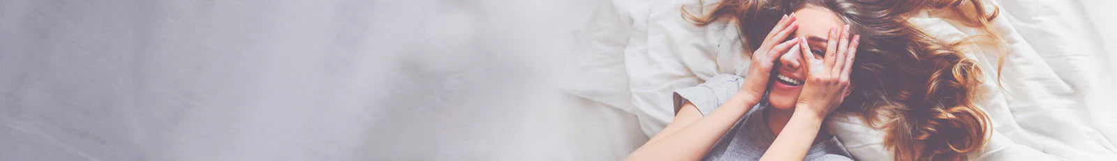 Person lying on a bed with hands covering face, possibly indicating sadness or distress.