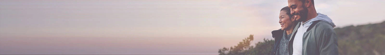 Two people standing on a hillside at sunset with a blurred background