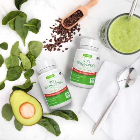 Two bottles of Iron Bisglycinate supplements with a green smoothie, avocado, and spinach on a white background.
