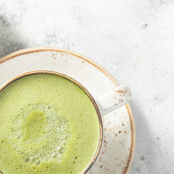 Cup of green tea with foam on a light gray background