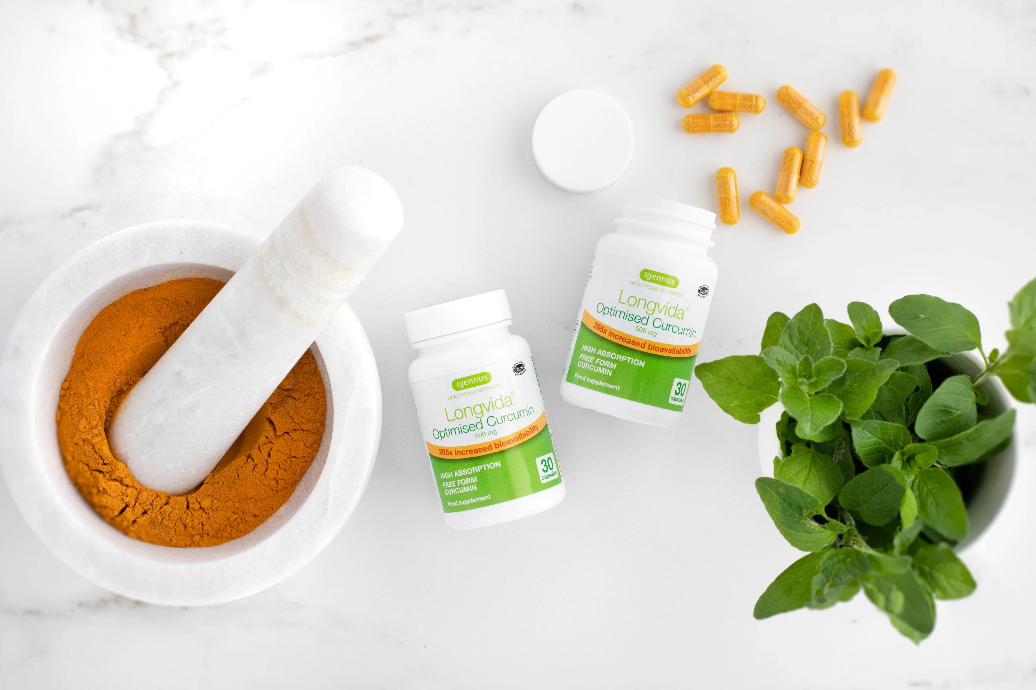 Supplement bottles, a mortar and pestle with brown powder, and a plant on a white surface.