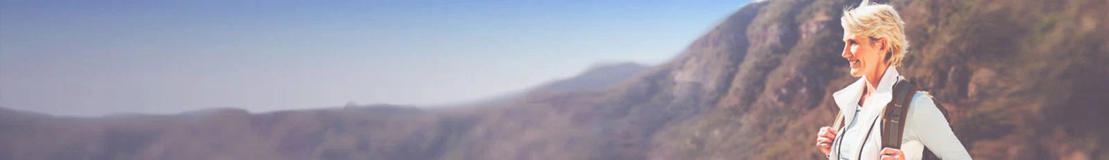 Person with a backpack standing on a mountain trail with scenic views.