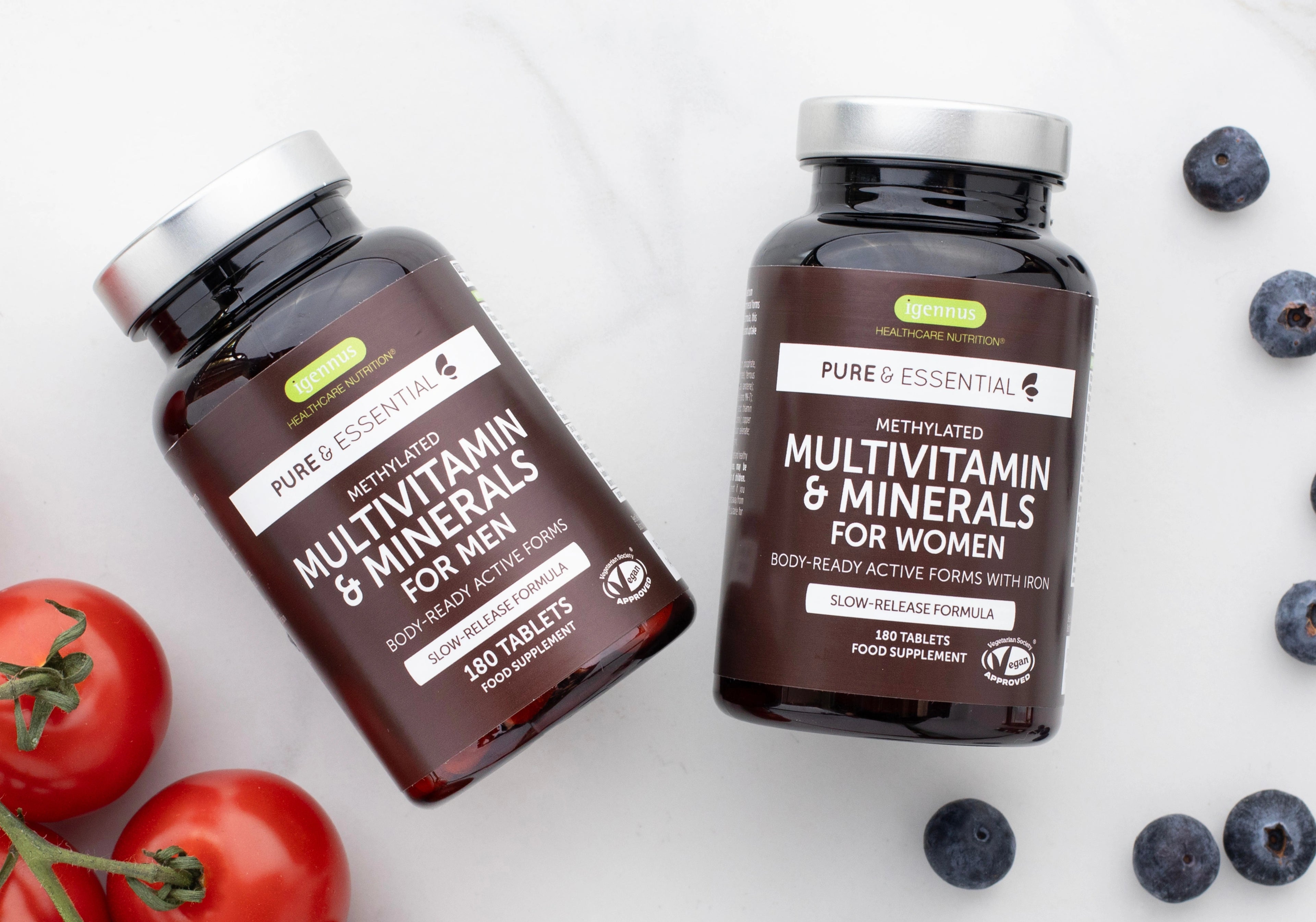 Two bottles of Pure Essential multivitamin supplements for men and women on a white background with tomatoes and blueberries.