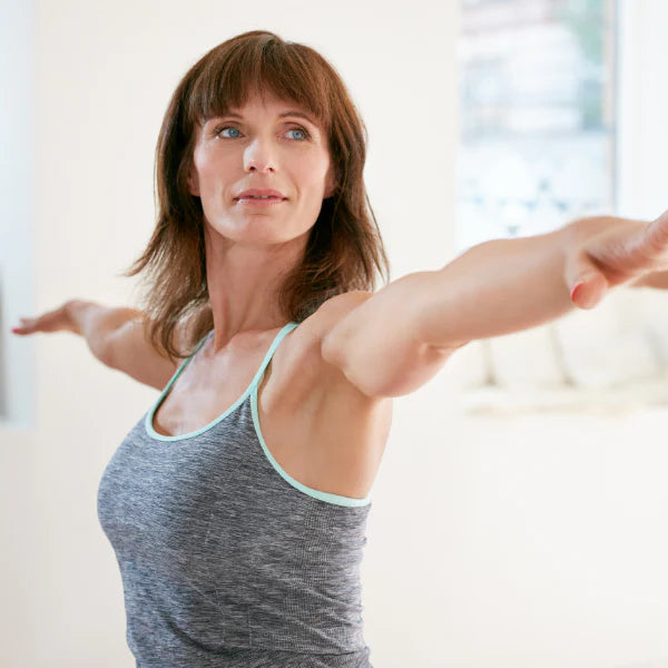 Woman in a gray tank top stretching her arms in a bright room