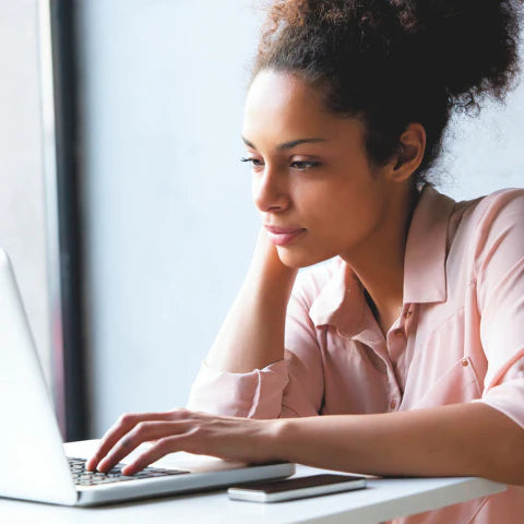 Woman using a laptop at a desk with a blurred background