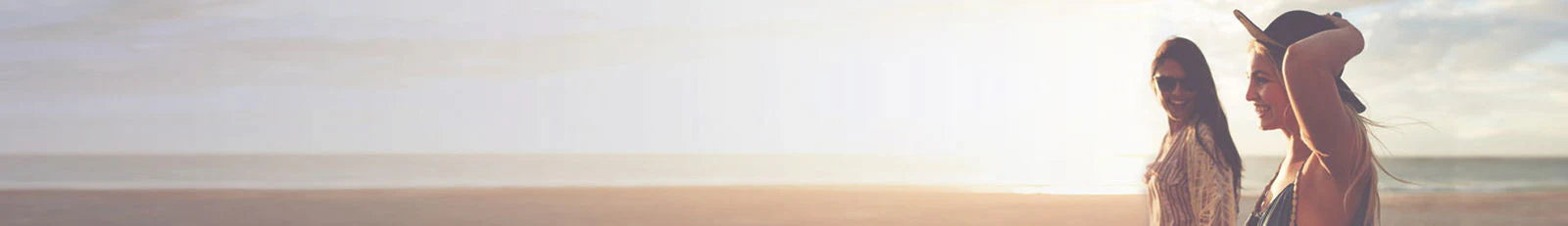Two women standing on a beach at sunset, with the ocean in the background.