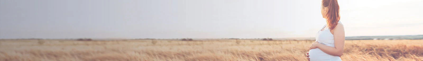 Pregnant woman standing in a field with a plain background