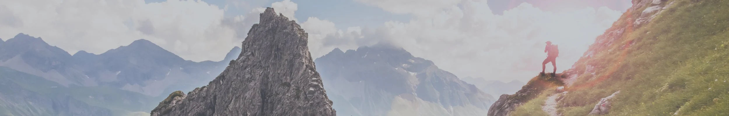 Person standing on a mountain peak with a scenic view of mountains in the background