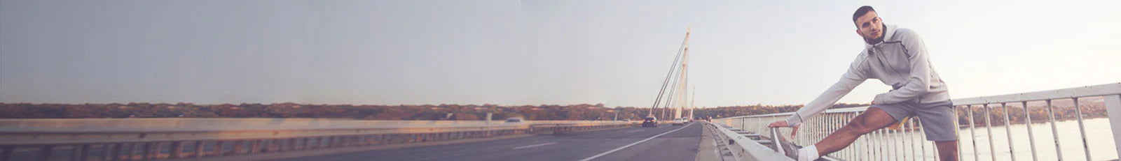 Man stretching on a bridge with a clear sky and road in the background