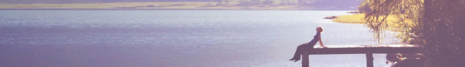 Person sitting on a wooden pier overlooking a calm lake with a blurred background