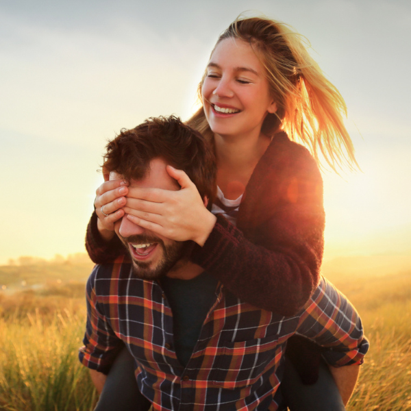 Man giving a piggyback ride to a woman in a field at sunset