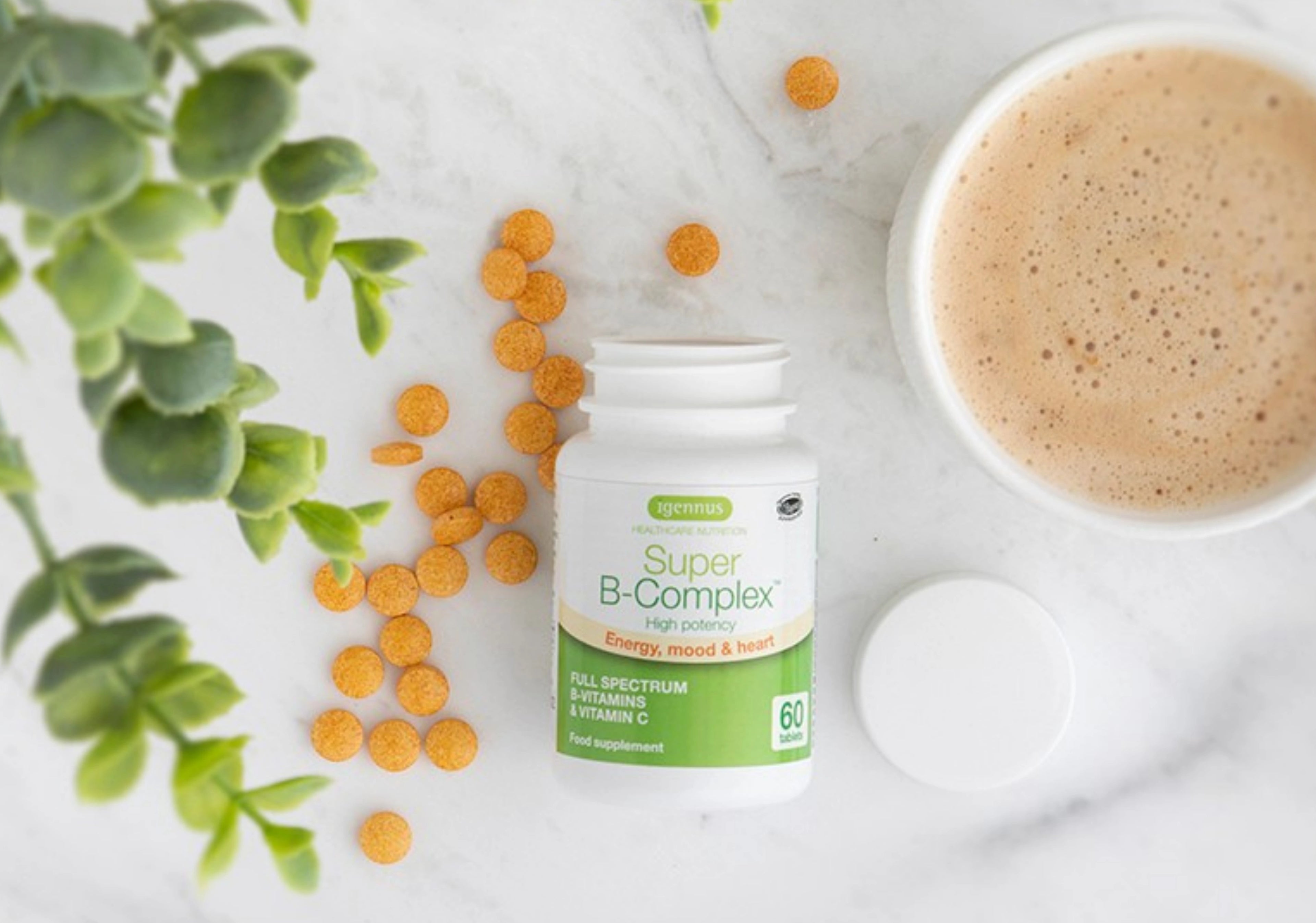 Supplement bottle labeled 'Super B-Complex' with scattered capsules on a light surface with a plant and cup of coffee in the background.