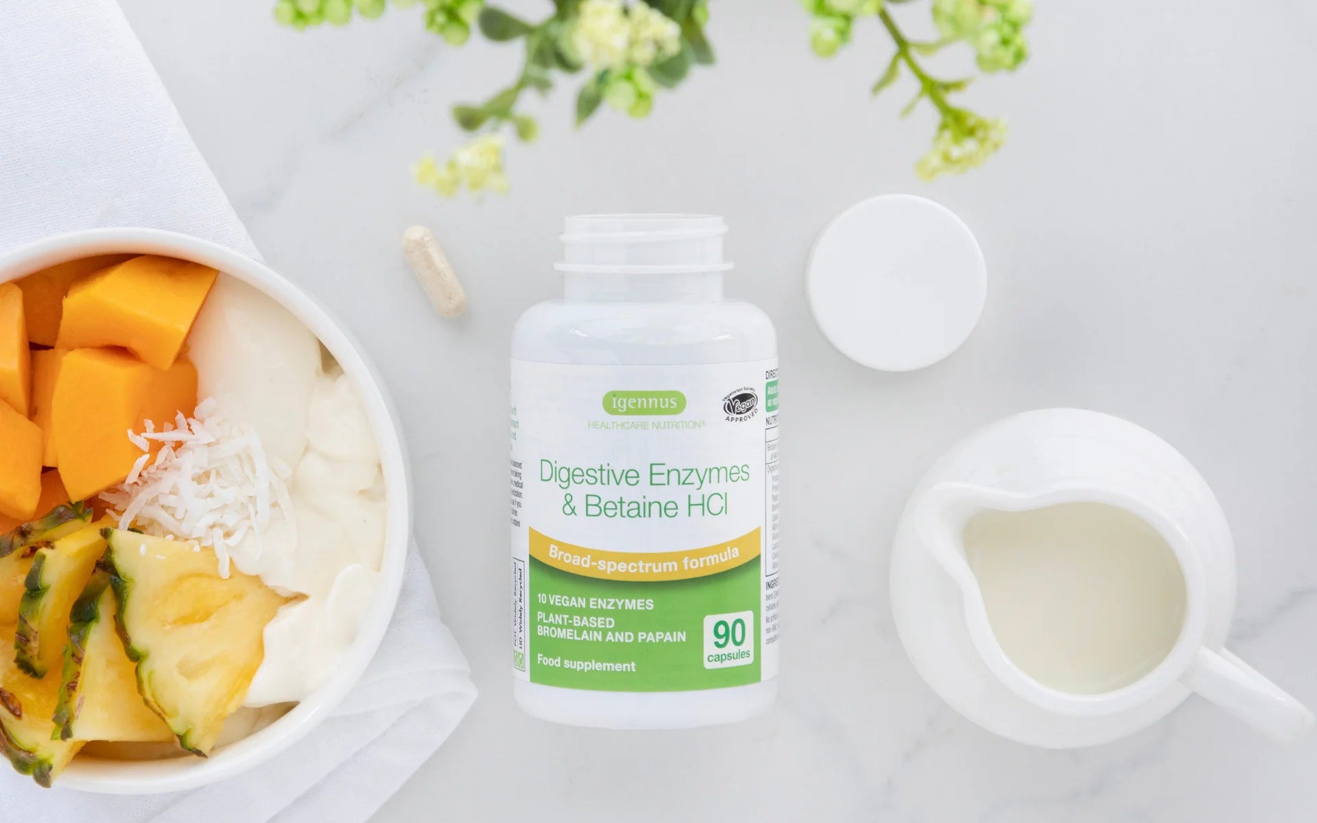 Supplement bottle labeled 'Digestive Enzymes & Betaine HCl' on a table with a bowl of fruit and a cup.