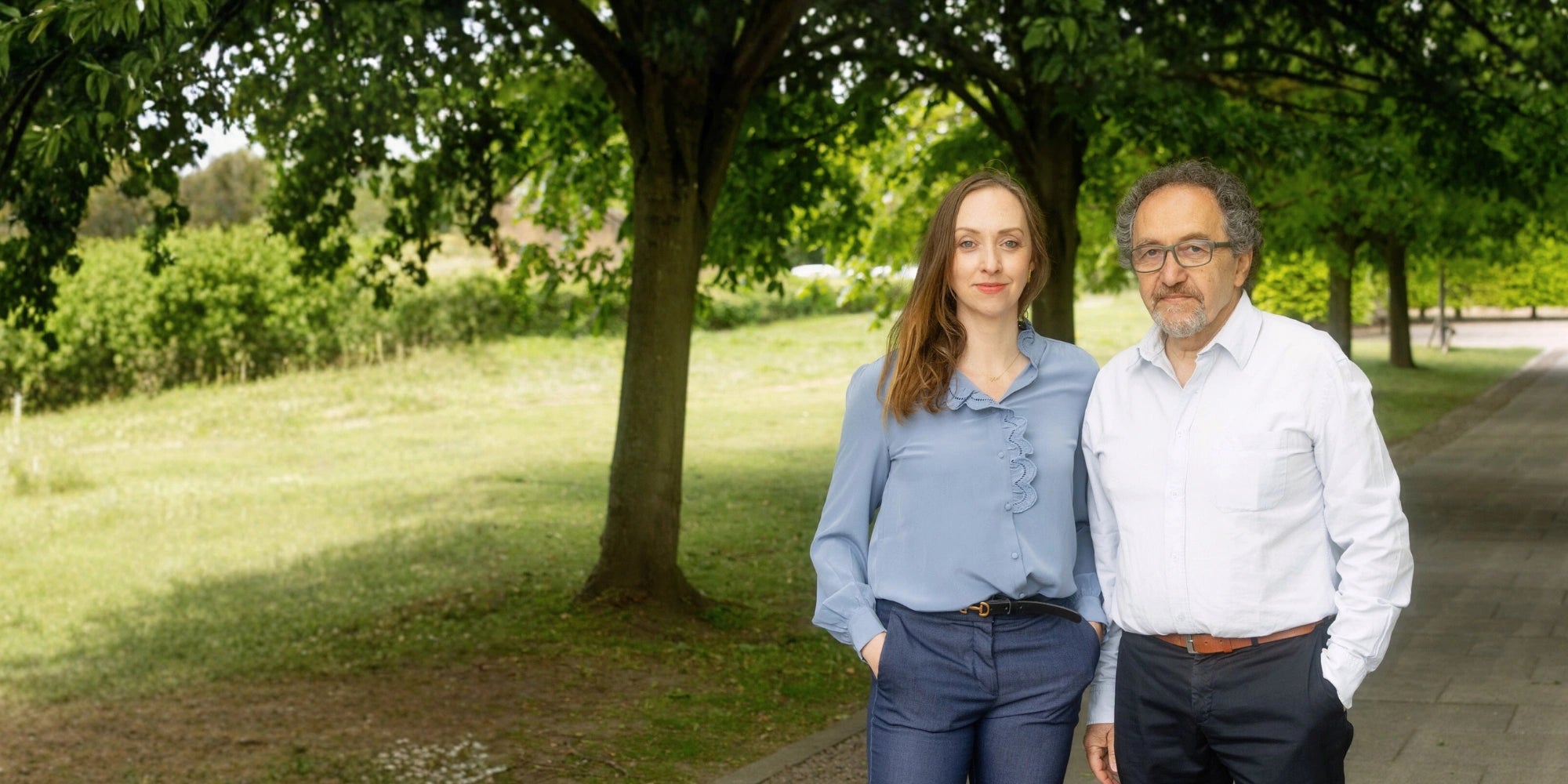 Two people standing in a park with trees and grass in the background