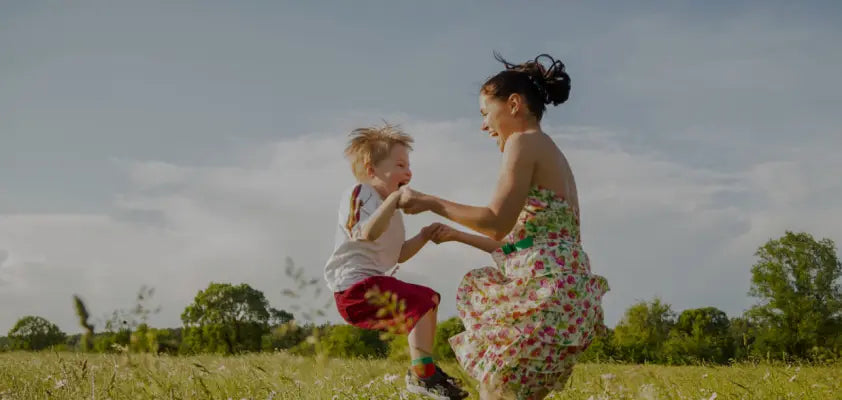 Woman and child playing in a grassy field with trees and blue sky in the background