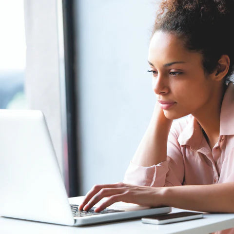 Woman using a laptop at a desk with a blurred background