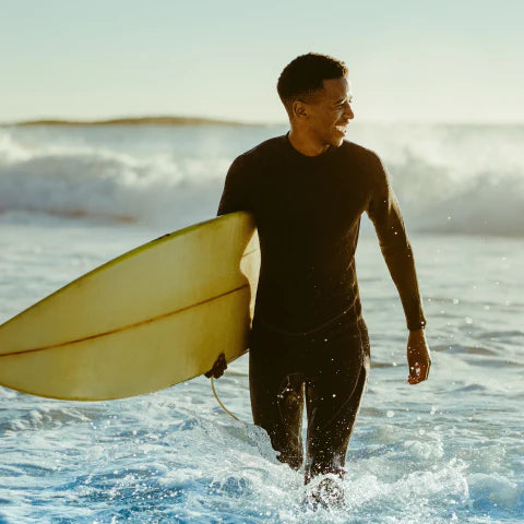 Man in a wetsuit holding a surfboard walking out of the ocean.