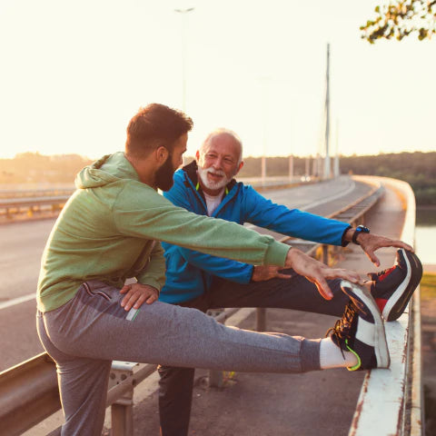 Two men stretching on a road during sunset