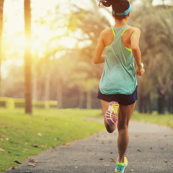 Woman running on a path in a park with trees and sunlight in the background