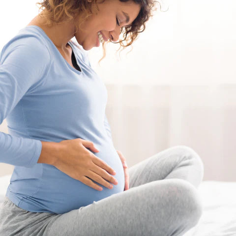 Pregnant woman in a blue shirt and gray pants sitting on a white couch.