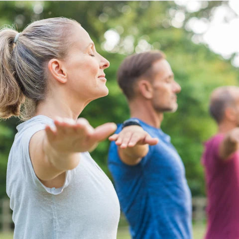Two people practicing yoga outdoors with a blurred background of greenery