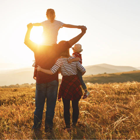 Family of four standing in a field with sunset in the background