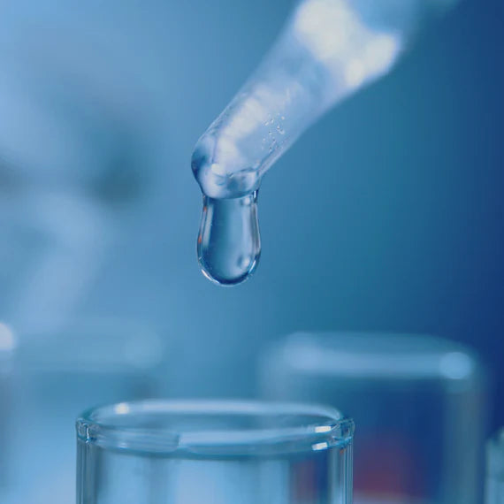 Dropper with a drop of liquid approaching a test tube against a blue background