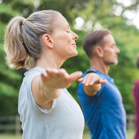 Two people practicing yoga outdoors with trees in the background