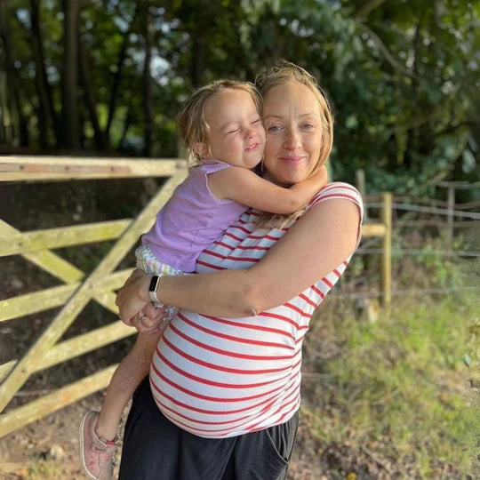 Woman holding a young child outdoors with a wooden fence and trees in the background