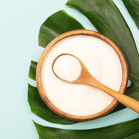 Coconut oil in a wooden bowl with a spoon on green leaves against a light blue background
