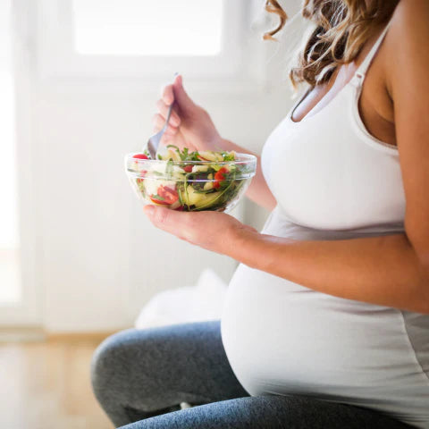 Pregnant woman holding a bowl of salad indoors
