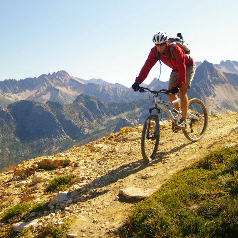 Person mountain biking on a trail with mountains in the background