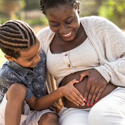 Woman with a child touching her pregnant belly outdoors