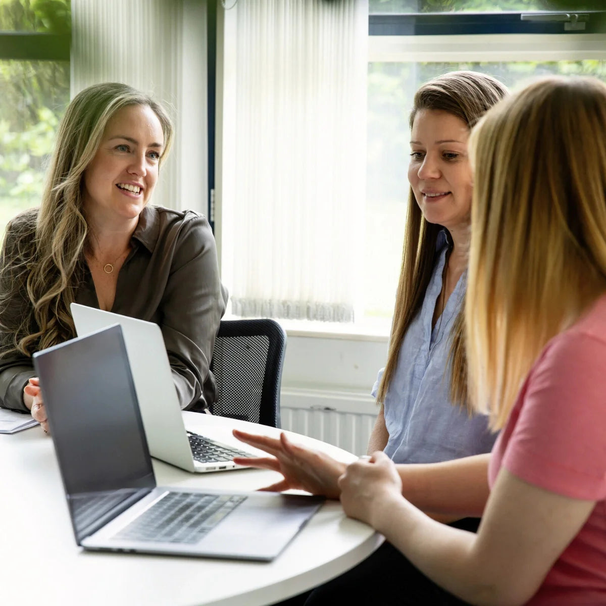 Three women sitting at a table with laptops, engaged in a discussion.
