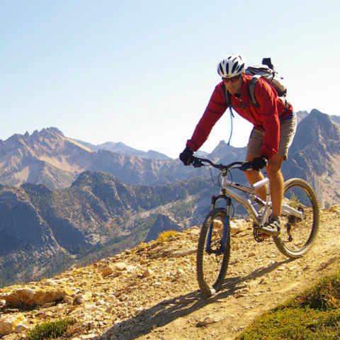 Person mountain biking on a trail with mountains in the background