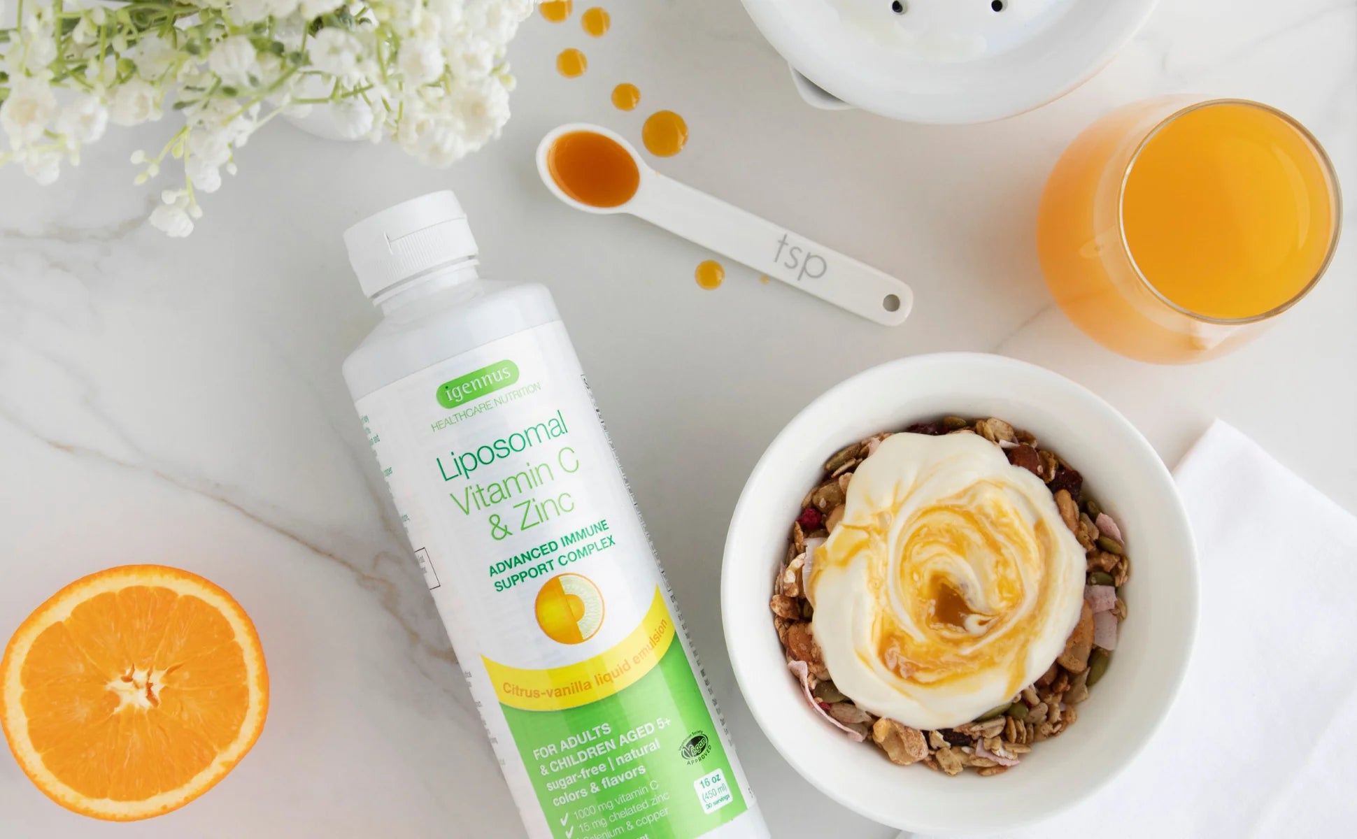 Liposomal Vitamin C and Zinc supplement bottle with a bowl of yogurt and granola, orange slices, and a measuring spoon on a white surface.