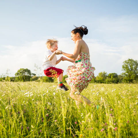 Woman and child playing in a grassy field with trees in the background