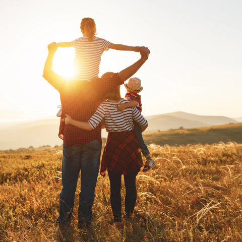 Family of four standing in a field with sunset in the background