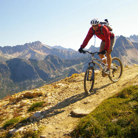 Person mountain biking on a trail with mountains in the background