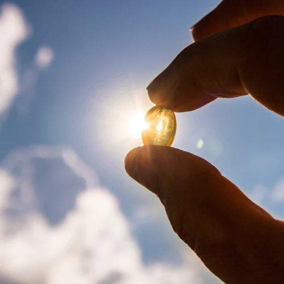 Hand holding a capsule against a bright sky