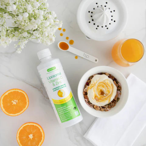 Liposomal Vitamin C & Zinc bottle with oranges, a bowl of yogurt, and flowers on a white surface.