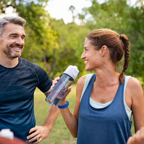 Man and woman outdoors, man handing water bottle to woman