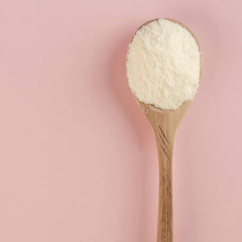 Wooden spoon filled with white powder on a pink background