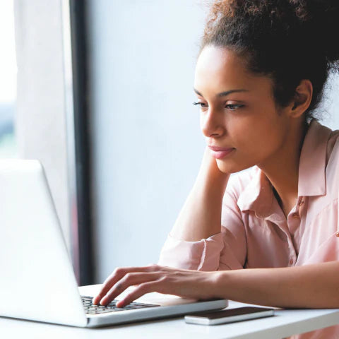Woman using a laptop at a desk with a blurred background