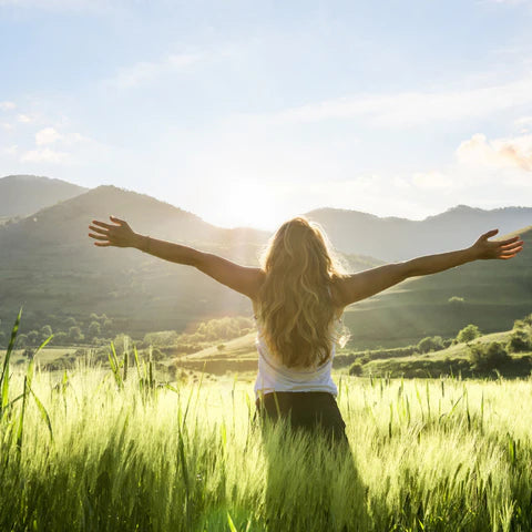 Person with arms outstretched in a field with mountains in the background
