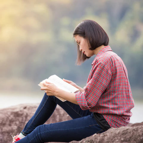 Woman reading a book outdoors by a lake
