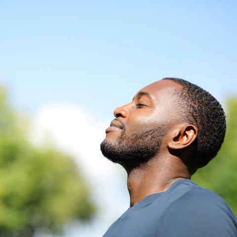 Man with eyes closed against a blue sky and green trees